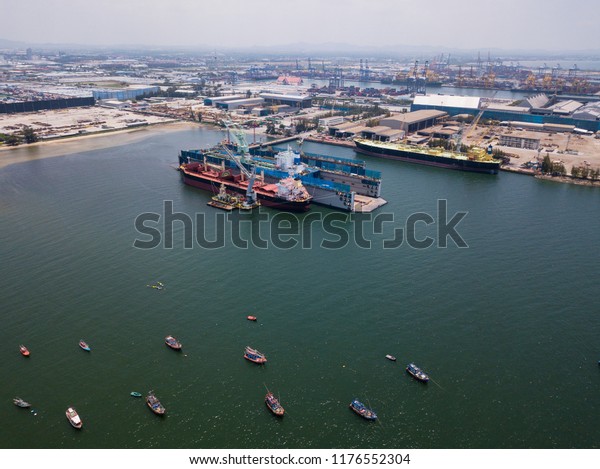 Aerial view of logistics concept floating dry\
dock servicing cargo ship and commercial vehicles, cars and pickup\
trucks waiting to be load on to a roll-on/roll-off car carrier ship\
at Laem Chabang