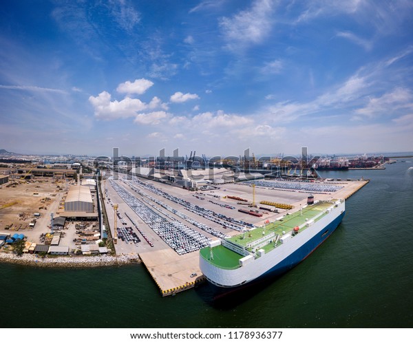 Aerial view of logistics concept floating dry dock\
servicing cargo ship and commercial vehicles, cars and pickup\
trucks waiting to be load on to a roll-on/roll-off car carrier ship\
at Laem Chabang doc