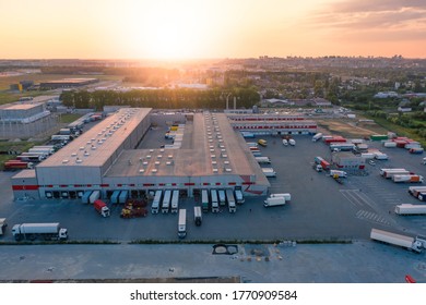 Aerial view of the logistics park with warehouse, loading hub and many semi trucks with cargo trailers standing at the ramps for load/unload goods at sunset