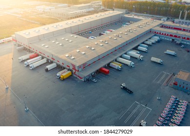 Aerial view of a logistics park with warehouse, loading hub and many semi trucks with cargo trailers standing at the ramps for load/unload goods at sunset. 