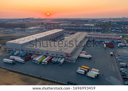 Aerial view of the logistics park with warehouse, loading hub and many semi trucks with cargo trailers standing at the ramps for load/unload goods at sunset