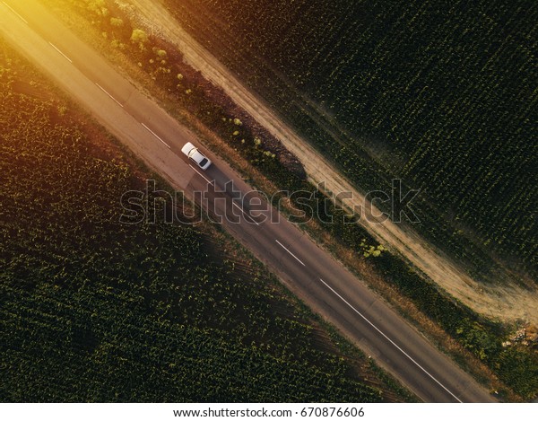 Aerial view of lonely car on the road driving\
towards sunset, drone point of\
view