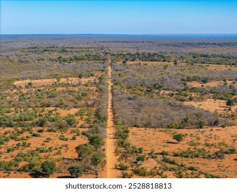 Aerial view of a long dirt road cutting through a dry, semi-arid landscape, showcasing the expansive and remote wilderness, with scattered vegetation and clear skies in a rural African setting. - Powered by Shutterstock