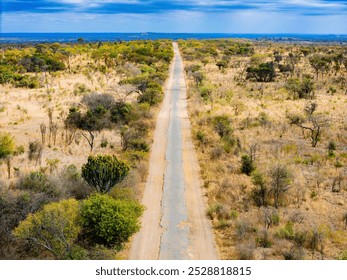 Aerial view of a long dirt road cutting through a dry, semi-arid landscape, showcasing the expansive and remote wilderness, with scattered vegetation and clear skies in a rural African setting. - Powered by Shutterstock