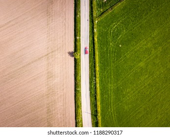 Aerial View Looking Down On A Rural Road In The UK Countryside With A Car Racing Along It. On A Bright Sunny Day, Farmland And Crops Can Be Seen Either Side Of The Road