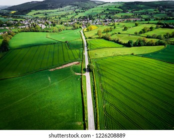 Aerial view looking down on a rural road in the UK countryside. On a bright sunny day, farmland and crops can be seen either side of the road