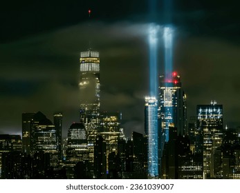 Aerial view of low lying clouds positioned in front of the Freedom Tower in New York City at night, while the tribute in light beams are illuminated.
