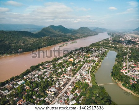 Aerial view of Luang Prabang and surrounding lush mountains of Laos. The Nam Kahn River, a tributary of the Mekong River, flows peacefully on the right.