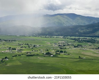 Aerial View Of Lush, Green Farmland, Fields, Homes, Hills And Mountains In Missoula Area, Montana, USA. Rain Clouds Overhead