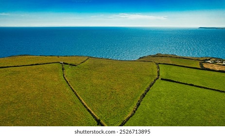 Aerial view of lush green fields meeting the blue ocean under a clear sky. In Cornwall, UK. - Powered by Shutterstock