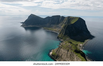 An aerial view of a lush, green peninsula in the blue Atlantic Ocean, seen from the island of Vaeroy in the Lofoten islands in Norway  - Powered by Shutterstock