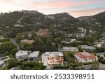 Aerial view of a luxurious residential neighborhood in a hilly area at sunset, showcasing modern and classic houses surrounded by lush greenery.