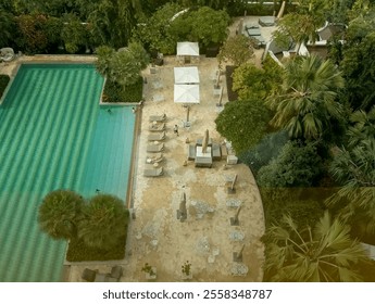 an aerial view of a luxurious resort pool area with sun loungers, umbrellas, and lush tropical landscaping - Powered by Shutterstock