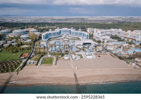 Aerial view of a luxury beachfront resort with pools, water park, lush gardens, and a sandy beach, surrounded by greenery and modern architecture.