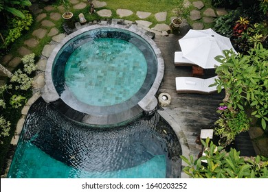 Aerial View Of Luxury Round Pool With White Umbrellas And Sun Beds In Tropical Jungle And Palm Trees. Luxurious Villa, Swimming Pool In Forest, Ubud, Bali