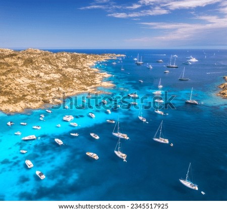 Aerial view of luxury yachts and boats on sea bay in sunny summer day. Travel in Sardinia, Italy. Drone view from above of speed boats, yachts, sea lagoon, rocky coast, transparent water. Top view