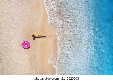 Aerial view of the lying beautiful young woman with pink swim ring on the sandy beach near sea with waves at sunset. Summer vacation in Lefkada island, Greece. Top view of sexy girl, clear blue water - Shutterstock ID 2145323503