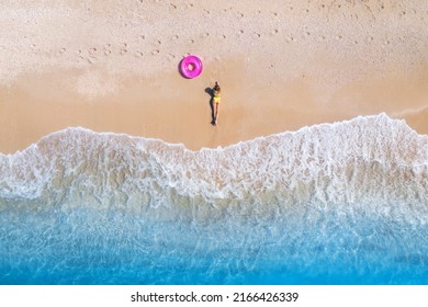Aerial view of the lying beautiful young woman with pink swim ring on the sandy beach near sea with waves at sunset. Summer vacation in Lefkada island, Greece. Top view of sexy girl, clear blue water - Shutterstock ID 2166426339