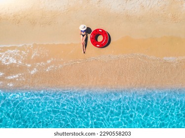 Aerial view of a lying woman in hat with red swim ring on sandy beach and blue sea at sunset in summer. Tropical landscape with girl, clear water, waves. Top view. Vacation in Sardinia island, Italy	 - Powered by Shutterstock