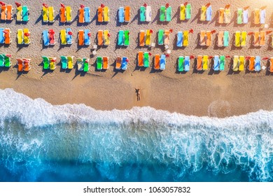 Aerial view of lying woman on the beach with colorful chaise-lounges. Beautiful young woman on the sea at sunset in Oludeniz, Turkey. Top view. Seascape with girl, azure water and waves. Holiday