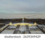 An aerial view of the majestic Peterhof Palace with its formal gardens covered in snow, overlooking the frozen Gulf of Finland
