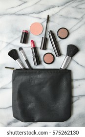 Aerial View Of Make Up Products Spilling Out Of A Black Cosmetics Bag, On A White Marble Counter Top Background