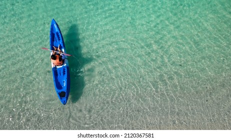 Aerial View Of Man In Floating Kayak. Kayaking Out From Beach On Clear Blue Sea. Right Side Copy Space. Water Sports And Summer Recreations. Person With Life Jacket On Boat.