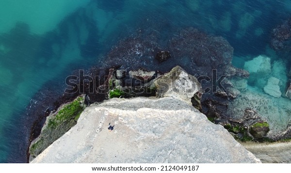 Aerial view of a man on the edge of the precipice\
of a cliff overlooking the\
sea