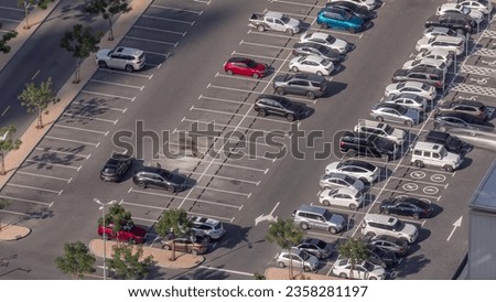 Aerial view of many colorful cars parked on parking lot with lines and markings for parking places and directions timelapse. Green trees. Dubai