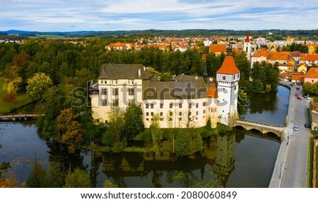 Aerial view of medieval Blatna water castle surrounded parks and lakes on background with cityscape on autumn day, South Bohemian Region, Czech Republic..