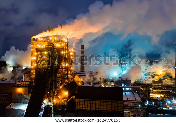Aerial\
view of metallurgical plant blast furnace at night with smokestacks\
and fire blazing out of the pipe. Industrial panoramic landmark\
with blast furnance of metallurgical\
production