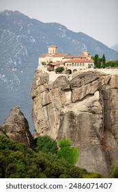 Aerial view of Meteora Monastery complex on rocks, illuminated by rising sun against mountains in background. UNESCO World Heritage Site. Greece.