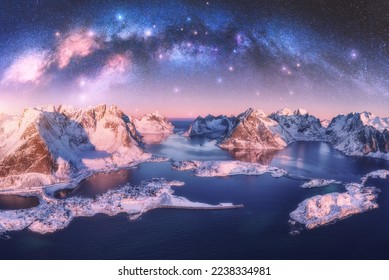 Aerial view of Milky Way arch, sea, village and snow covered mountains in winter at night. Lofoten Islands, Norway. Arctic landscape with pink starry sky, road, houses, milky way, snowy rocks. Space - Powered by Shutterstock