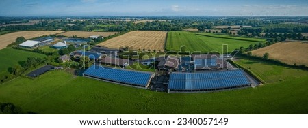 Aerial view of modern agriculture livestock farm with photovoltaic panels on the roofs of barn, agricultural fields with corn, biogas plant. View of livestock farm with renewable energy.