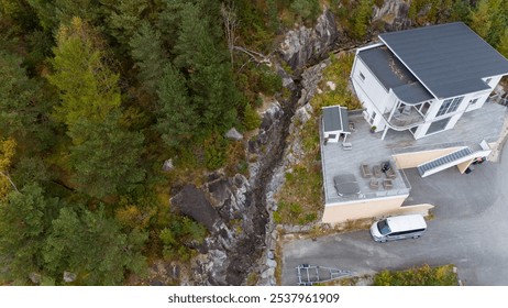 Aerial view of a modern building surrounded by dense forest and a rocky stream. - Powered by Shutterstock