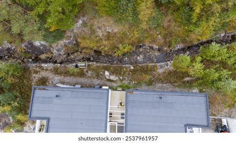 Aerial view of a modern building surrounded by dense forest and a rocky stream. - Powered by Shutterstock