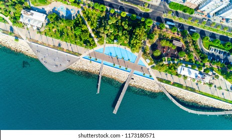 Aerial view of Molos Promenade park on coast of Limassol city centre,Cyprus. Bird's eye view of the jetty, beachfront walk path, palm trees, Mediterranean sea, piers, urban skyline and port from above