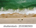 An aerial view of Montauk Beach with green waves and people under yellow umbrellas.