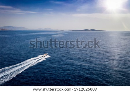 Aerial view of a motor yacht traveling over blue sea towards an island on the horizon