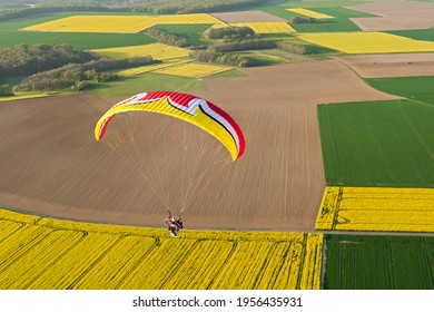 Aerial view of a motorized paraglider flying over yellow rapeseed canola fields in spring. Essonne department, Ile-de-France region, France