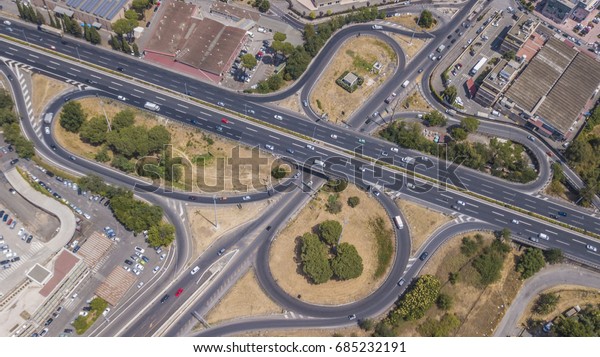 Aerial view of a motorway exit in\
rome. Cars run fast along the highway while some are entering or\
exiting the accelerating lane or deceleration\
lane.