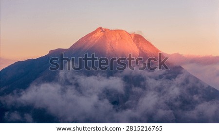 Aerial view of Mount Merapi illuminated by golden hour light with clouds drifting around its slopes in Kecamatan Dukun, Jawa Tengah, Indonesia