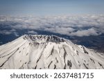Aerial view of Mount St. Helens covered in snow, with a backdrop of clouds and blue sky in Washington, USA.