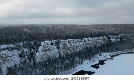 Aerial view of mountain cliff and river. Clip. Frosty cold snowy morning and the endless evergreen pine forest. - Powered by Shutterstock