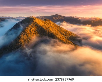 Aerial view of mountain peak in low clouds at sunrise in autumn. Top drone view of hills with red and orange trees in fog, colorful sky in fall. Slovenia. Nature. Mountain valley. Autumn forest. Alps - Powered by Shutterstock