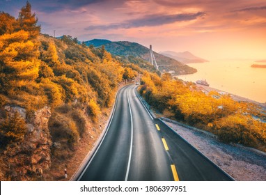 Aerial view of mountain road and beautiful orange forest at colorful sunset in autumn. Dubrovnik, Croatia. Top view of road, trees, sea, mountain, red sky in fall. Landscape with highway and sea coast