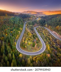 Aerial View Of Mountain Road In Forest At Sunset In Autumn. Top View From Drone Of Road In Woods. Beautiful Landscape With Roadway In Hills, Pine Trees, Mountains, Golden Sunlight In Fall. Travel