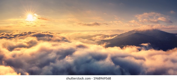 Aerial view of mountains in orange clouds at sunrise in summer. Mountain peak in fog. Beautiful landscape with rocks, hills, sky. Top view from drone. Mountain valley in low clouds. View from above - Shutterstock ID 1968969568