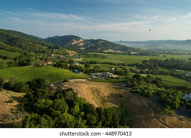 Aerial view of multicolored hot air balloons floating in blue sky above Northern California vineyards