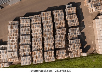 Aerial view of neatly arranged shipping containers or crates in a storage yard. The containers are stacked in rows, showcasing a variety of colors and textures. - Powered by Shutterstock